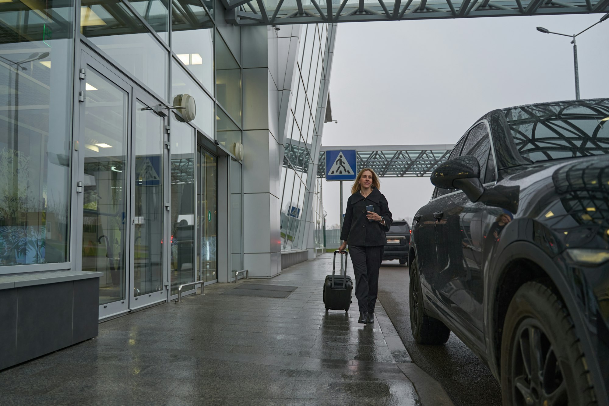 Woman with suitcase going to a car near airport entrance